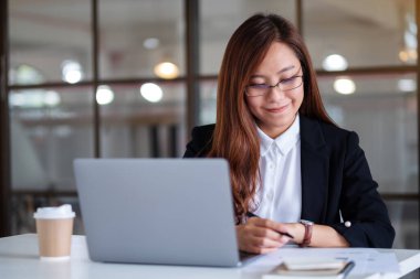 Not defterine yazan ve ofiste çalışırken dizüstü bilgisayar kullanan iş kadınının yakın plan resmi