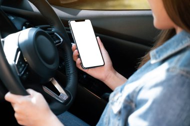 Araba kullanırken cep telefonu tutan ve kullanan bir kadının görüntüsü.