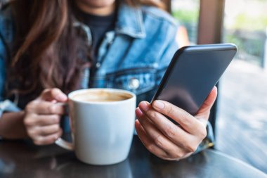 Kahve içerken cep telefonu kullanan bir kadının yakın plan görüntüsü.