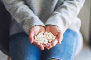 Beyaz ilaç kapsüllerini elinde tutan bir kadının yakın plan fotoğrafı.