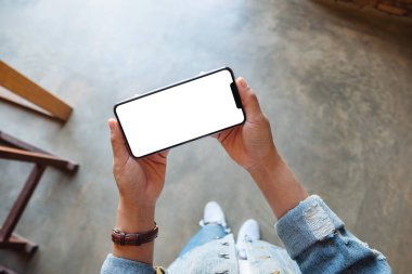 Üst görünüm, elinde beyaz ekranlı siyah cep telefonu olan bir kadının görüntüsü. 