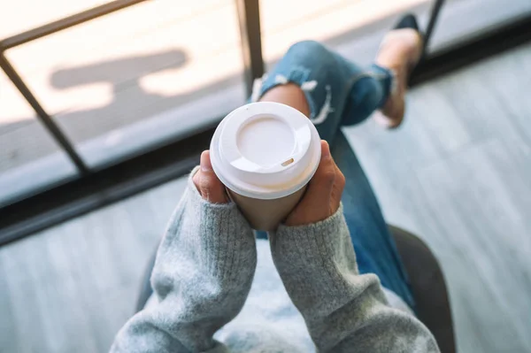 Top view image of a woman sitting and holding a paper cup of hot coffee in the morning