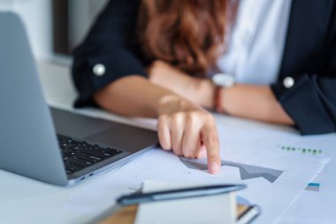 Ofiste dizüstü bilgisayarla çalışırken iş kadınının evrak işleriyle uğraşırken çekilmiş yakın plan resmi.