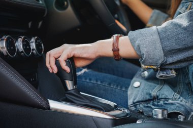 Yakından bakınca, araba sürerken otomatik vites kolu değiştiren bir kadın sürücü görülüyor.
