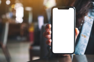 Kafede elinde siyah cep telefonu tutan ve gösteren bir kadının görüntüsü.