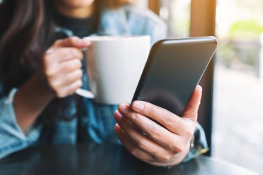 Kahve içerken cep telefonu kullanan bir kadının yakın plan görüntüsü.