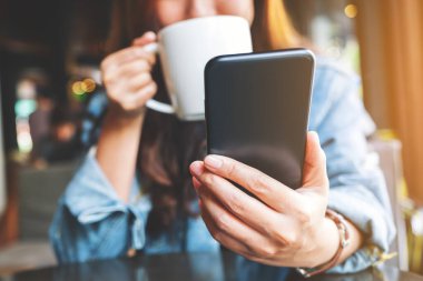 Kahve içerken cep telefonu kullanan bir kadının yakın plan görüntüsü.