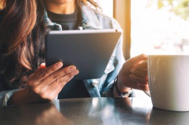 Kahve içerken elinde tablet tablet kullanan bir kadının yakın plan görüntüsü