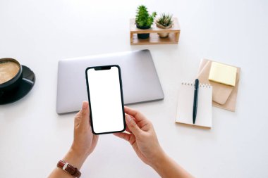 Ofisteki masada boş ekranlı ve dizüstü bilgisayarlı cep telefonu tutan ellerin en iyi görüntüsü.