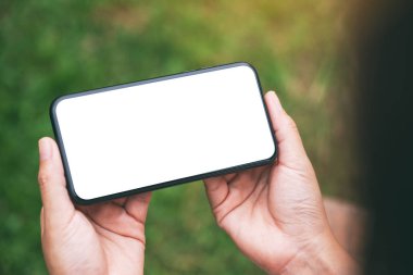 Yeşil doğa arka planına sahip boş masaüstü ekranlı siyah cep telefonu tutan bir kadının görüntüsü