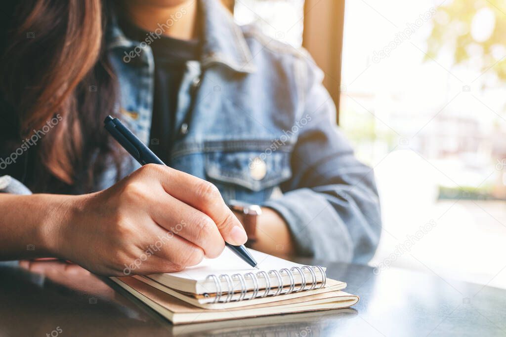 Closeup image of a woman writing on a blank notebook on the table 