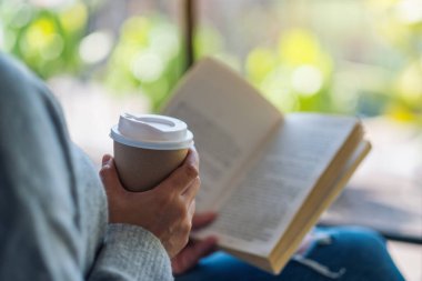 Kitap okuyan ve sabahları kahve içen bir kadının yakın plan görüntüsü.