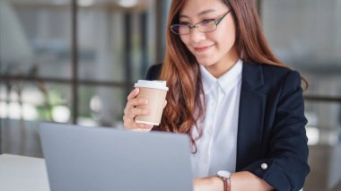İş kadınının ofiste çalışırken ve kahve içerken dizüstü bilgisayar kullanırken ve yazarken yakın plan görüntüsü