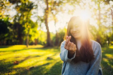 Güzel bir Asyalı kadın gün batımından önce parkta el işareti yapıyor.