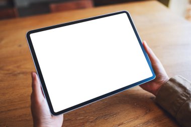 Ahşap masada beyaz ekranlı siyah tabletli bir kadının görüntüsü.