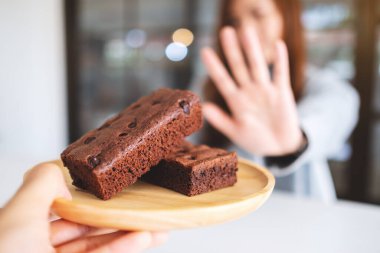 Tahta tabakta browni kekini reddetmek için el işareti yapan bir kadın.