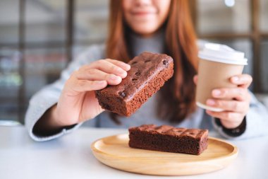 Kahve içerken elinde kek tutan ve yiyen güzel bir kadının yakın plan görüntüsü.