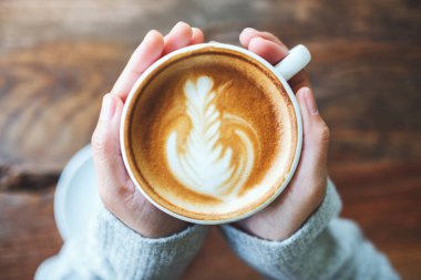 Tahta masada elinde bir fincan sıcak latte tutan bir kadının en iyi görüntüsü.