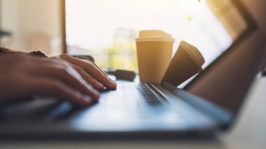 Masadaki dizüstü bilgisayarda çalışan ve yazan bir kadının ellerinin yakın plan görüntüsü.
