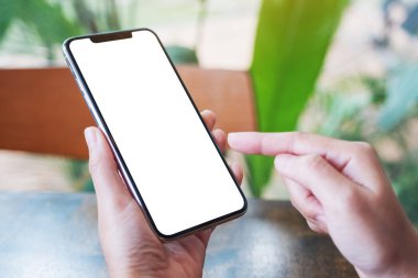 Boş masaüstü ekranı olan siyah bir cep telefonunu tutan ve işaret eden bir kadının görüntüsü 