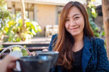 Kafede arkadaşlarıyla kahve bardaklarını tokuşturan Asyalı güzel bir kadının görüntüsünü kapat.