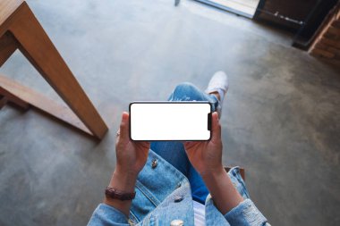 Kafede otururken elinde beyaz ekranlı siyah cep telefonu olan bir kadının üst görünüm görüntüsü