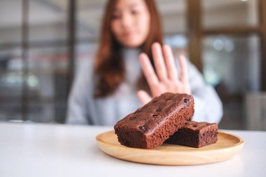 Tahta tabakta browni kekini reddetmek için el işareti yapan bir kadın.