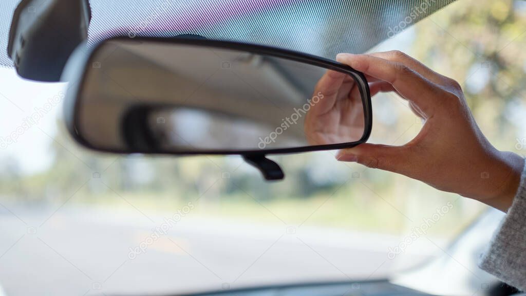 A woman adjusting a rear view mirror while driving car