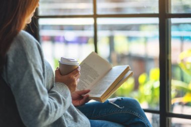 Kitap okuyan ve sabahları kahve içen bir kadının yakın plan görüntüsü.