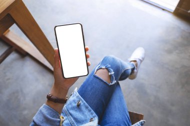 Kafede otururken elinde beyaz ekranlı siyah cep telefonu olan bir kadının üst görünüm görüntüsü