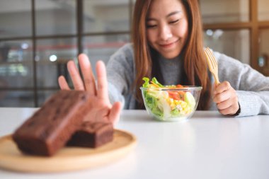Sebze salatası yemeyi seçen ve masadaki keki reddetmek için el işareti yapan bir kadın.