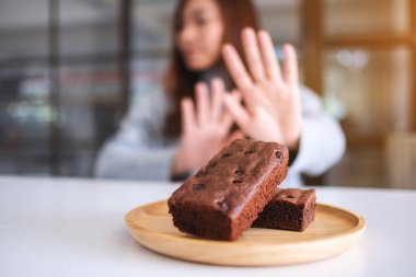 Tahta tabakta browni kekini reddetmek için el işareti yapan bir kadın.