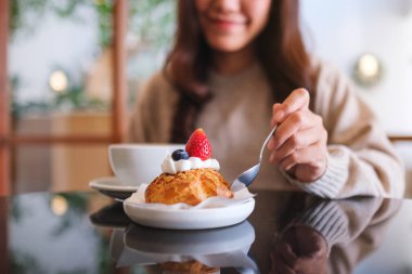 Çilekli choux krema yiyen ve kafede kahve içen bir kadının yakın plan görüntüsü.