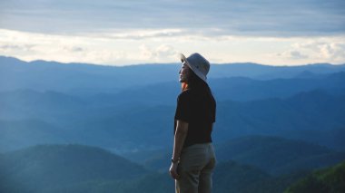 Dağ zirvesinde gün batımını izleyen bir kadının portresi.