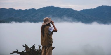 Yeşil bir dağ manzarası ve bulutlar denizinin fotoğrafını çeken bir kadın gezgin.