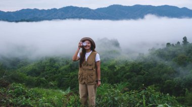 Yeşil bir dağ manzarası ve bulutlar denizinin fotoğrafını çeken bir kadın gezgin.