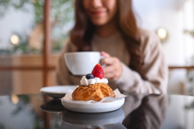 Kafede kahve içip çilekli krema yiyen bir kadının yakın plan görüntüsü.