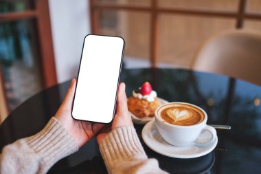 Kafedeki boş masaüstü ekranlı cep telefonu tutan ve kullanan bir kadının görüntüsü