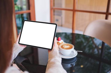 Kafede elinde boş beyaz masaüstü ekranı olan dijital tablet tutan bir kadının görüntüsü