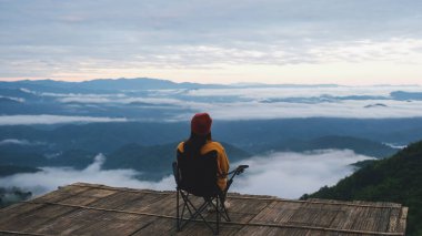 Güneş doğmadan önce oturup güzel sisli bir dağa bakan bir kadının arka görüntüsü.