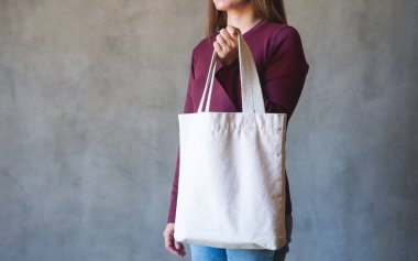 Yeniden kullanılabilir ve çevre kavramı için beyaz kumaş bir çanta taşıyan genç bir kadının yakın plan görüntüsü.