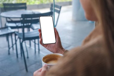 Kafede kahve içerken boş masaüstü ekran ile cep telefonu tutan ellerin görüntüsü