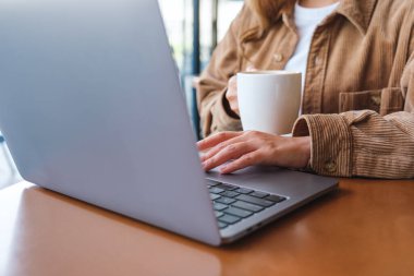 Kahve içerken dizüstü bilgisayar kullanan ve çalışan bir kadının yakın plan fotoğrafı.