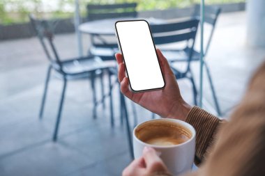 Kafede kahve içerken boş masaüstü ekran ile cep telefonu tutan ellerin görüntüsü