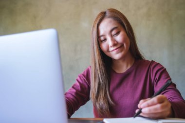 Dizüstü bilgisayarda çalışırken not defterine yazı yazan bir iş kadınının portre resmi