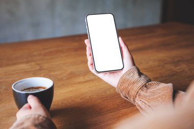 Kahve içerken boş masaüstü ekran ile cep telefonu tutan ellerin görüntüsü