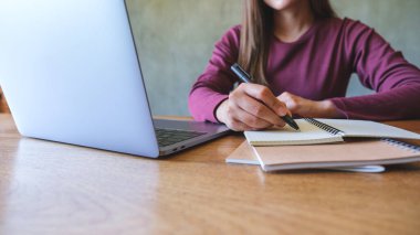 Dizüstü bilgisayarla uğraşırken not defterine yazan genç bir kadının yakın plan resmi