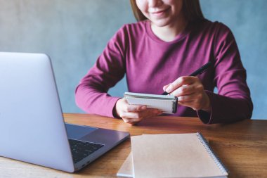 Dizüstü bilgisayarla uğraşırken not defterine yazan genç bir kadının yakın plan resmi