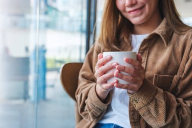 Kafede elinde sıcak kahve tutan ve içen genç bir kadının yakın plan görüntüsü.