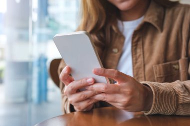 Kafede cep telefonu tutan ve kullanan genç bir kadının yakın plan görüntüsü.